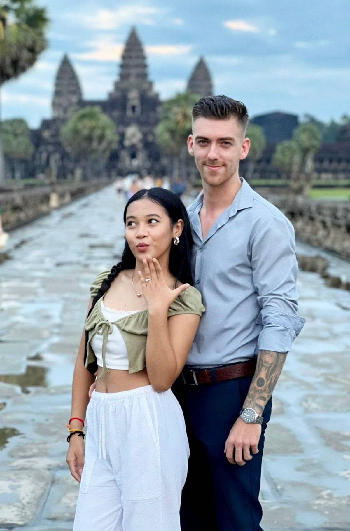 បុគ្គល​ម្នាក់​មាន​សក់​វែង និង​បុគ្គល​ម្នាក់​ទៀត​មាន​ស្នាម​សាក់​នៅ​ដៃ កំពុង​ឈរ​ក្បែរ​ប្រាសាទ​អង្គរវត្ត។