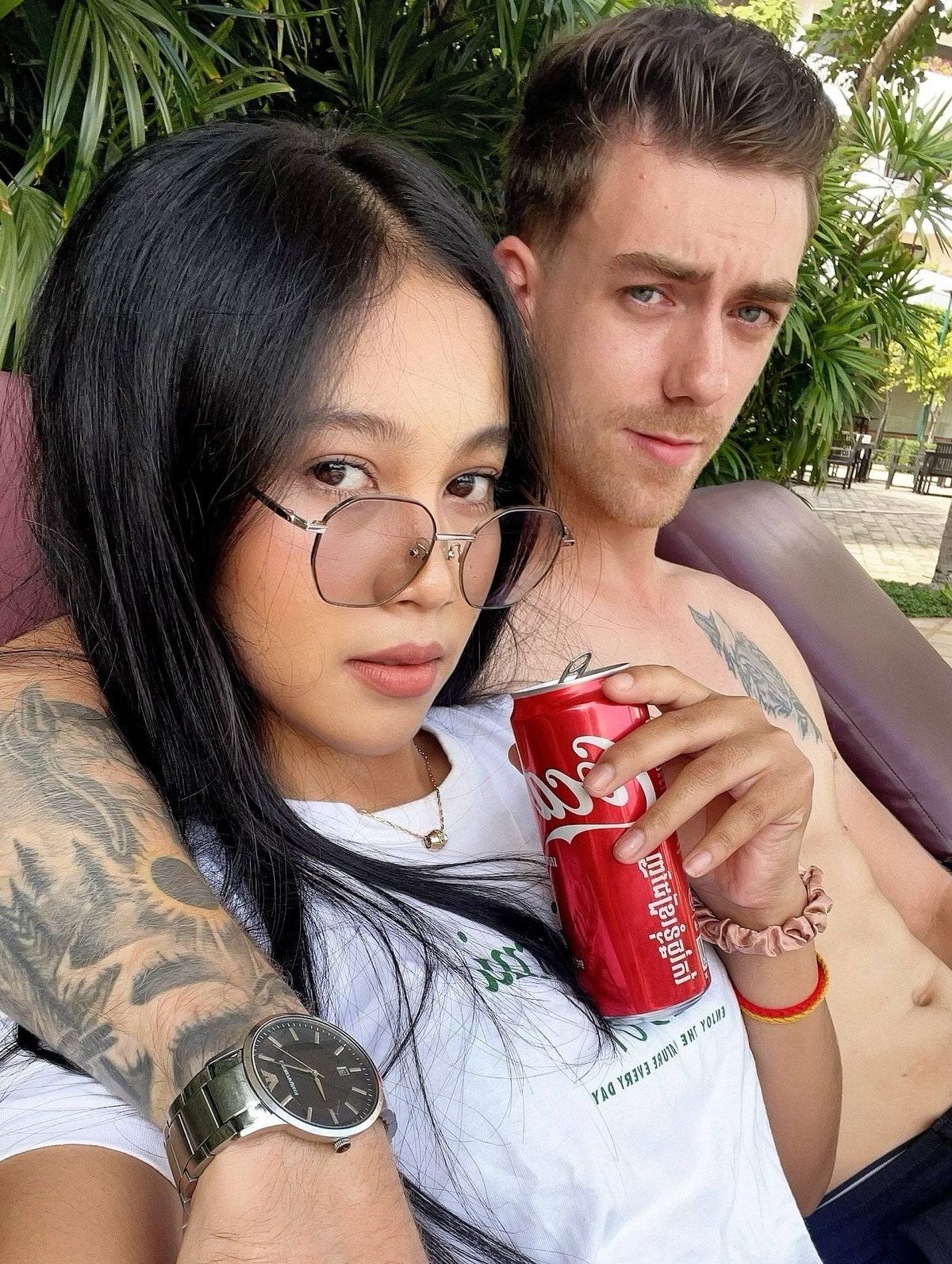 បុគ្គលពីរនាក់អង្គុយជិតគ្នានៅលើកៅអី ដោយមនុស្សម្នាក់កាន់កំប៉ុងពណ៌ក្រហម។ ស្ត្រី​នោះ​ពាក់​វ៉ែនតា និង​នាឡិកា ខណៈ​បុរស​នោះ​មាន​ស្នាម​សាក់​នៅ​លើ​ដៃ។ ពួកគេទាំងពីរកំពុងសម្លឹងមើលក្នុងទិសដៅតែមួយ ប្រហែលជាកំពុងជជែកគ្នាលេង ដោយមានផ្ទៃខាងក្រោយធម្មជាតិនៃរុក្ខជាតិបៃតងនៅពីក្រោយពួកគេ។